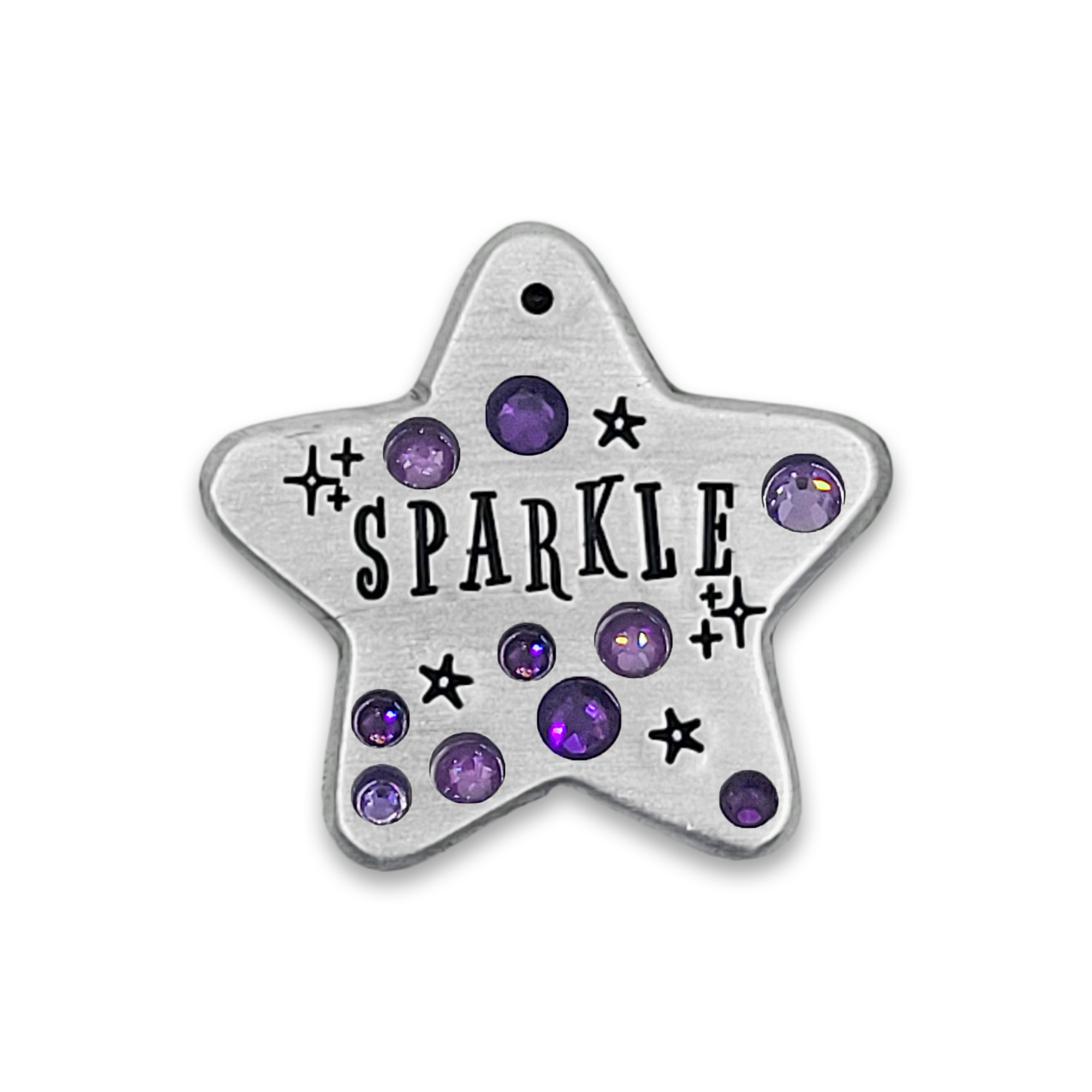 A silver toned metal star, stamped with the word "SPARKLE" and some little stars in black, set with sparkly purple crystals, all against a white background.