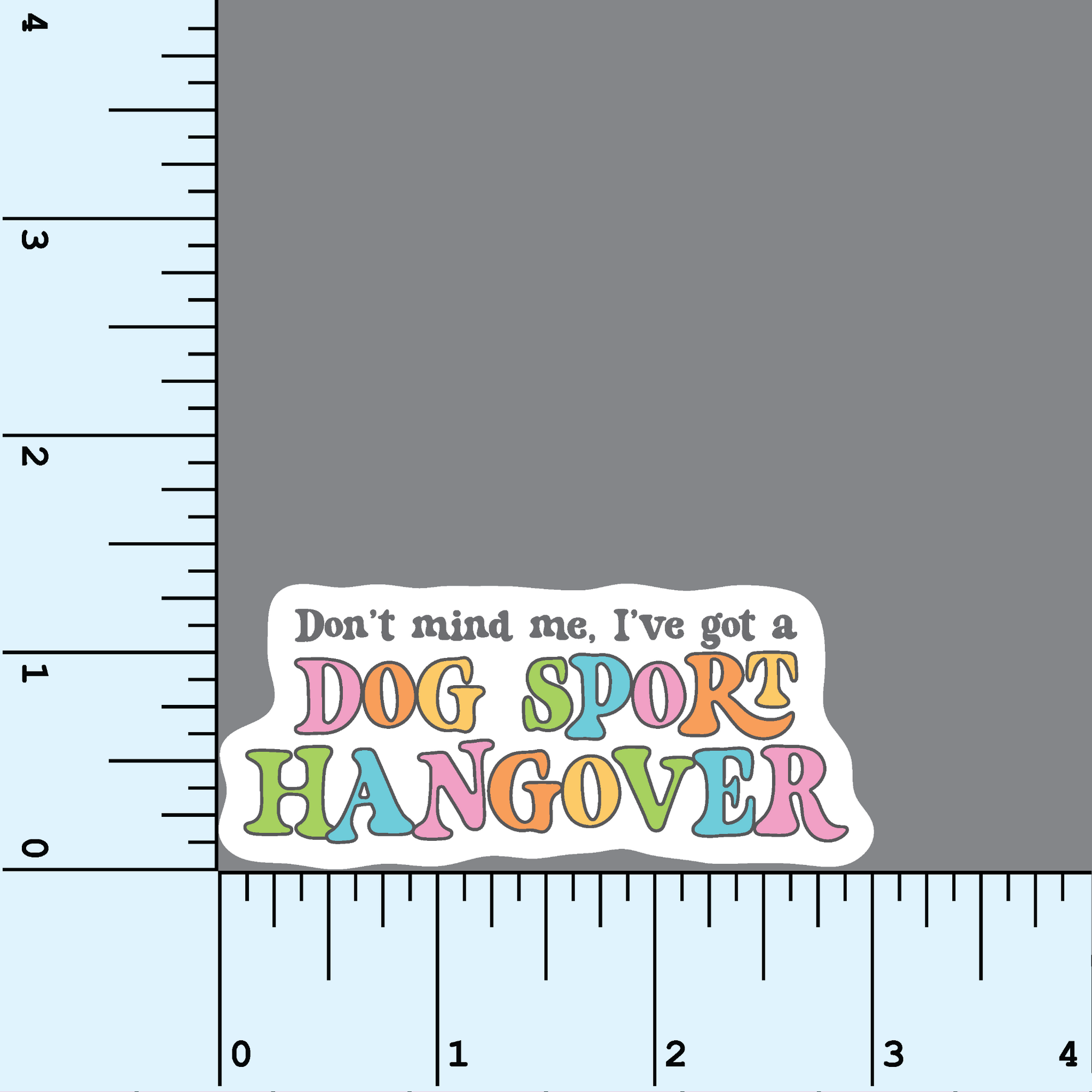 A sticker with colorful text stating &quot;don&#39;t mind me, I&#39;ve got a dog sport hangover&quot; in a fun retro style font shown beside a ruler to indicate 3&quot; size.