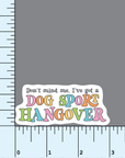 A sticker with colorful text stating "don't mind me, I've got a dog sport hangover" in a fun retro style font shown beside a ruler to indicate 3" size.