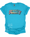 "Even My Dog Is A Feminist" printed in a pastel rainbow gradient in a vintage font on a laguna blue t-shirt.