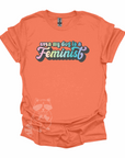 "Even My Dog Is A Feminist" printed in a pastel rainbow gradient in a vintage font on an orange t-shirt.