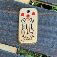 Load image into Gallery viewer, Rectangle brass pet tag with &quot;Bite Club&quot;, fangs, and 3 red crystals on a wood background. 
